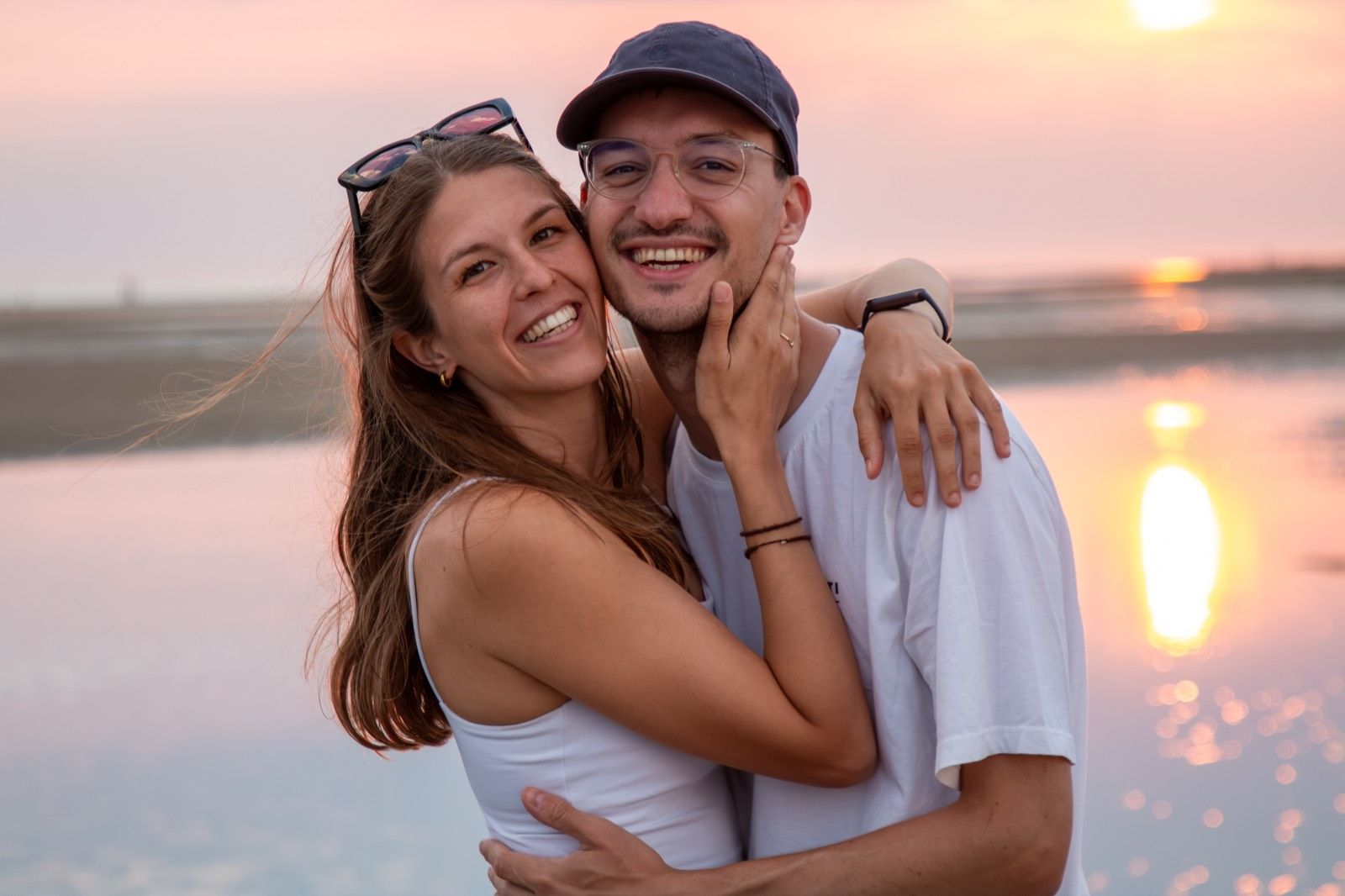 Vicky und Alex umarmen sich lachend am Wasser im Sonnenuntergang